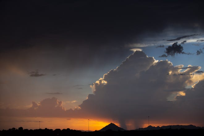 The sun sets behind Camelback Mountain and a monsoon storm, dropping rain over Phoenix on Aug. 23, 2018.