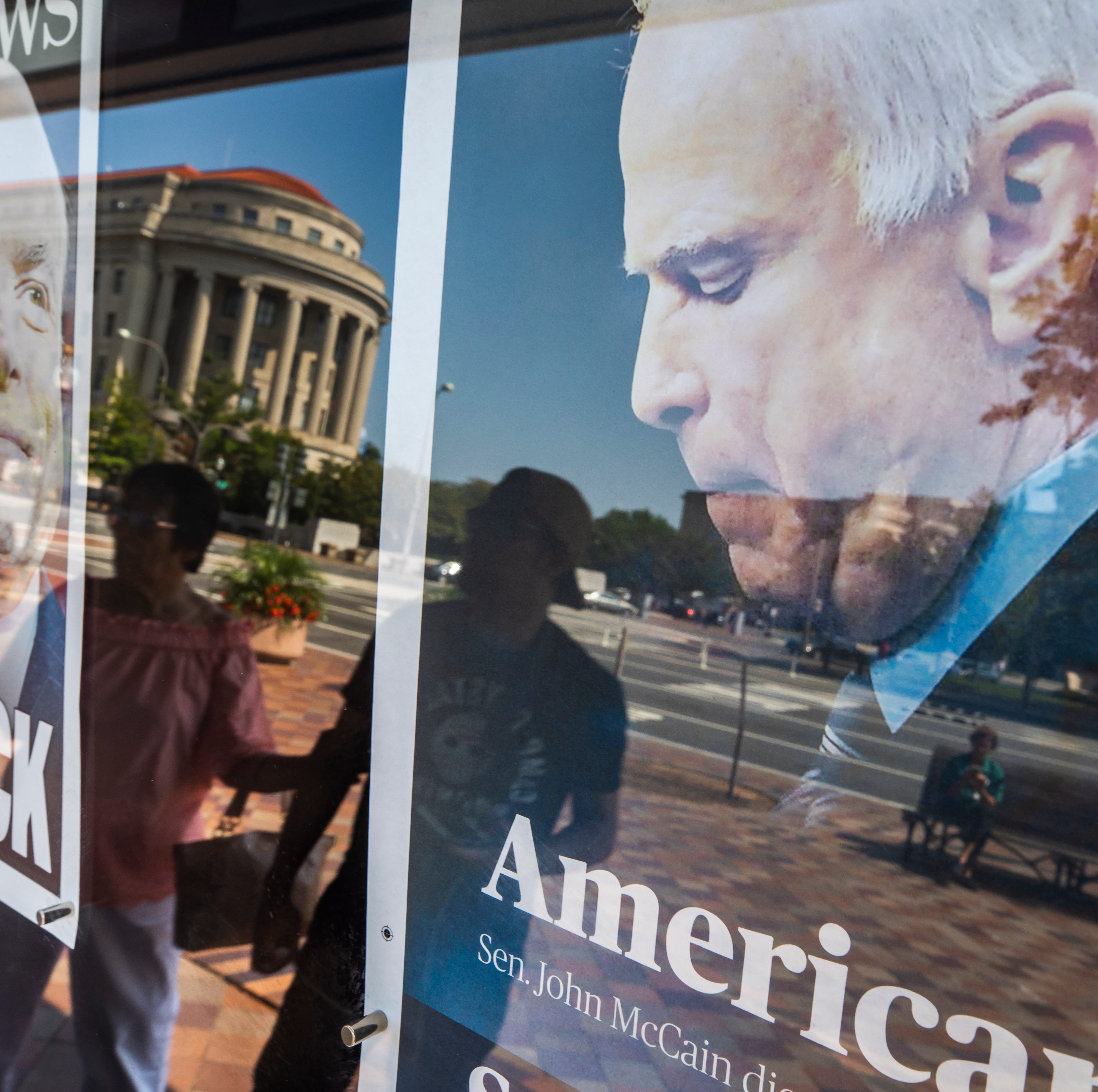 Pedestrians are reflected in the front page of the Fayetteville Observer, right, and the NY Daily News, which memorialize Republican Senator John McCain outside the Newseum in Washington, DC, on  Aug. 26, 2018.