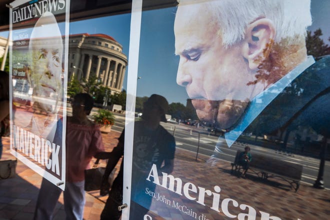 Pedestrians are reflected in the front page of the Fayetteville Observer, right, and the NY Daily News, which memorialize Republican Senator John McCain outside the Newseum in Washington, DC, on  Aug. 26, 2018. 