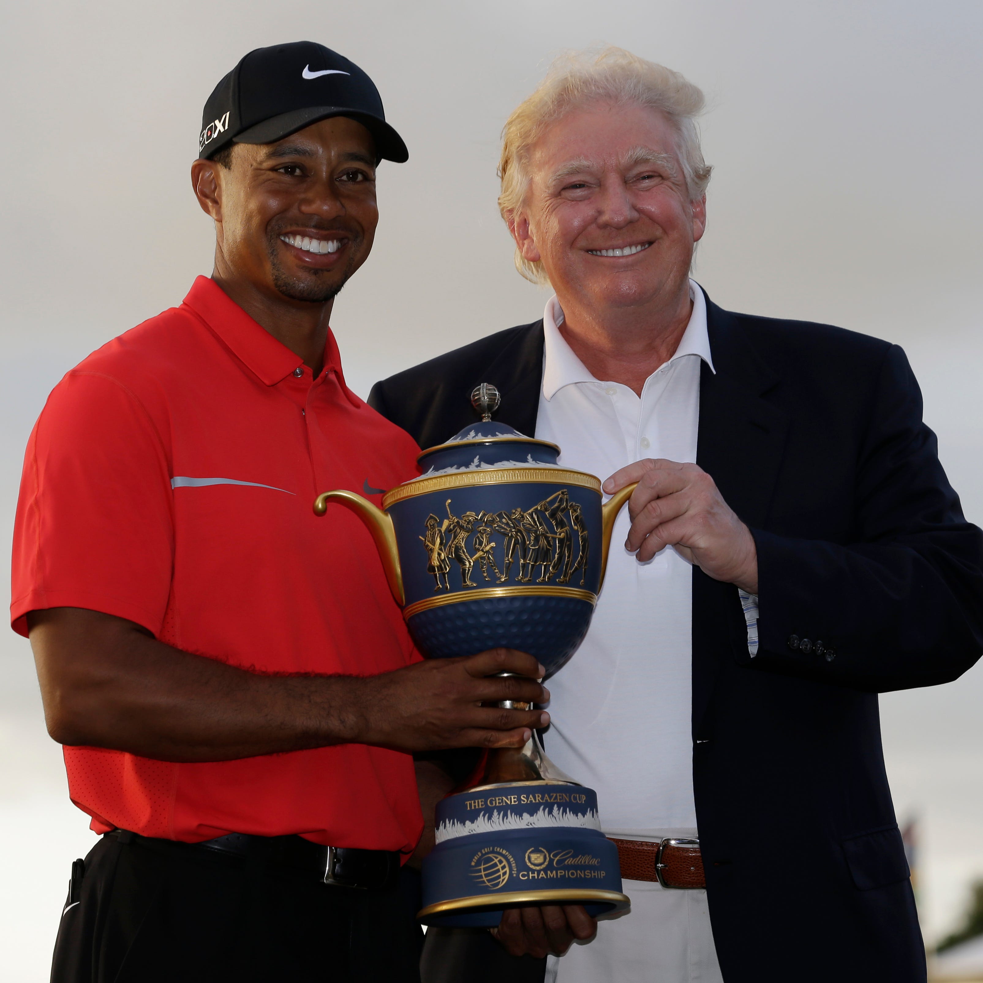 In a file photo from 2013, Tiger Woods stands with Donald Trump as he holds the Gene Serazen Cup for winning the Cadillac Championship in Doral, Fla.