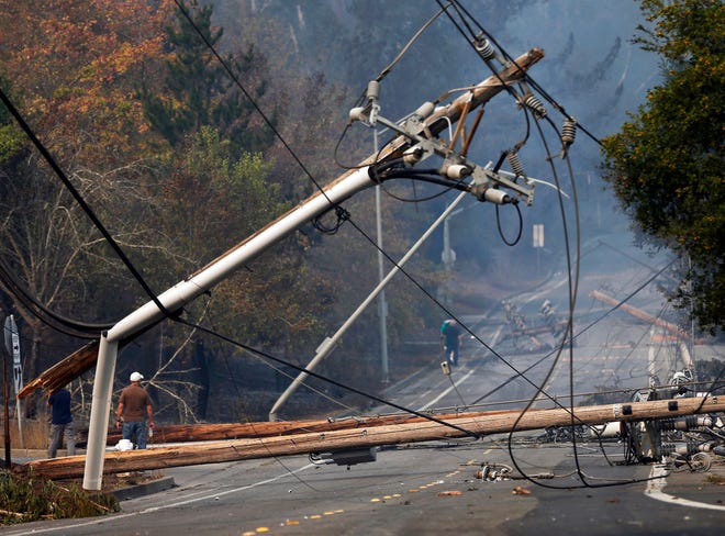 In this Oct. 10, 2017, file photo, people walk past a fallen transformer and downed power lines on Parker Hill Road in Santa Rosa. Utility workers won protections for their jobs, salaries, benefits and pensions as part of a measure allowing California power companies to raise electric bills to cover the cost of lawsuits from last year's deadly wildfires.