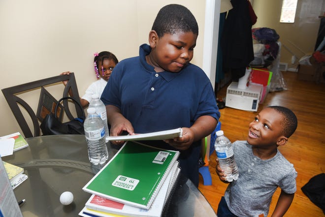 Adrian Nealy, left, gets his books and bottled water ready for school with his brother Rico, 3, and sister Cassidy, 4.  Detroit Public Schools Community District has alerted parents that only bottled water is available in the district until further notice.