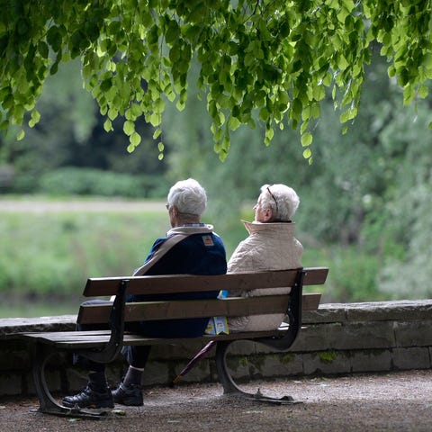 An elderly couple sits on a park bench.