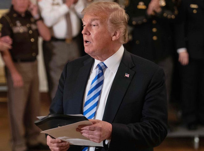 President Donald Trump reads from an article praising his administration as he answers a journalist during a meeting with sheriffs at the White House.