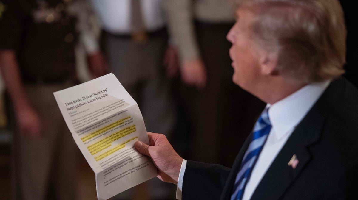 President Donald Trump reads an article praising his administration as he replies to a journalist during a meeting with sheriffs at the White House on Wednesday.