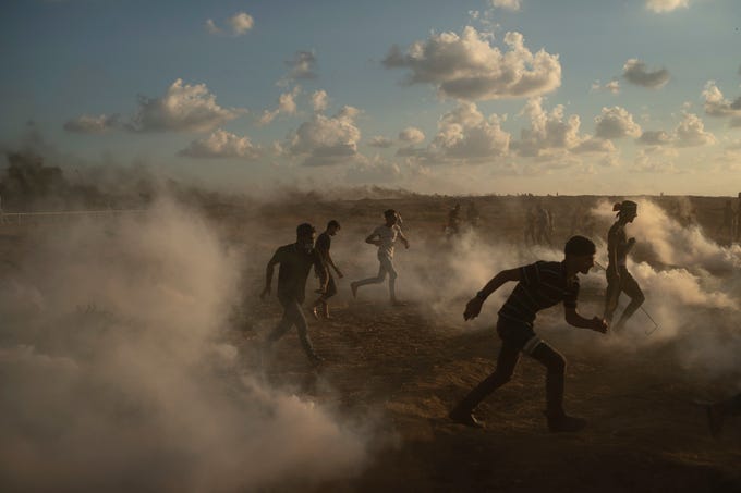 Palestinian protesters run from tear gas fired by Israeli troops during a protest at Gaza Strip's border with Israel, east of Gaza City, Friday, Sept. 7, 2018. A teenager was killed and dozens of other Palestinians injured by Israeli fire at a border protest, Gaza officials said.