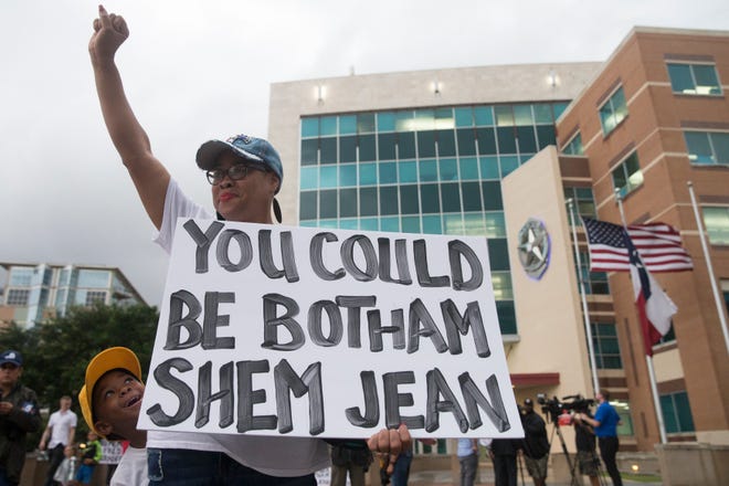 Pamela Grayson raises her fist as Solomon Grayson, 6, peaks behind her sign during a Mothers Against Police Brutality candlelight vigil for Botham Jean at the Jack Evans Police Headquarters on Sept. 7, 2018, in Dallas.