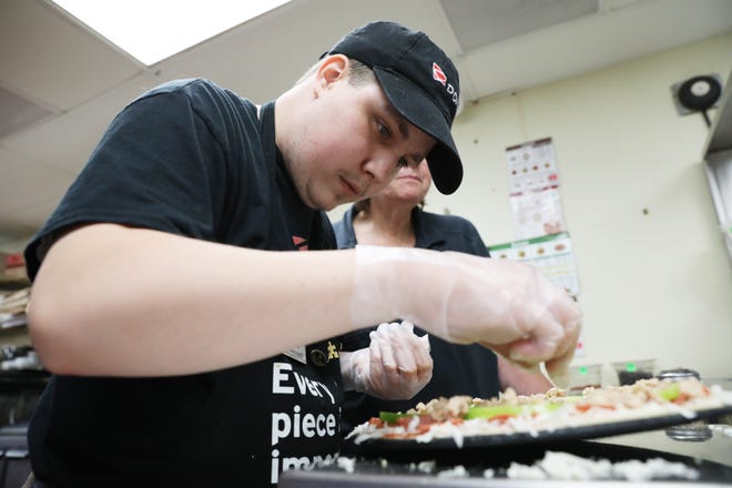 Jake Dewart makes a pizza at Donatos in Zanesville recently. Dewart, who was diagnosed with autism a the age of 3, have been working at Donatos for five years.