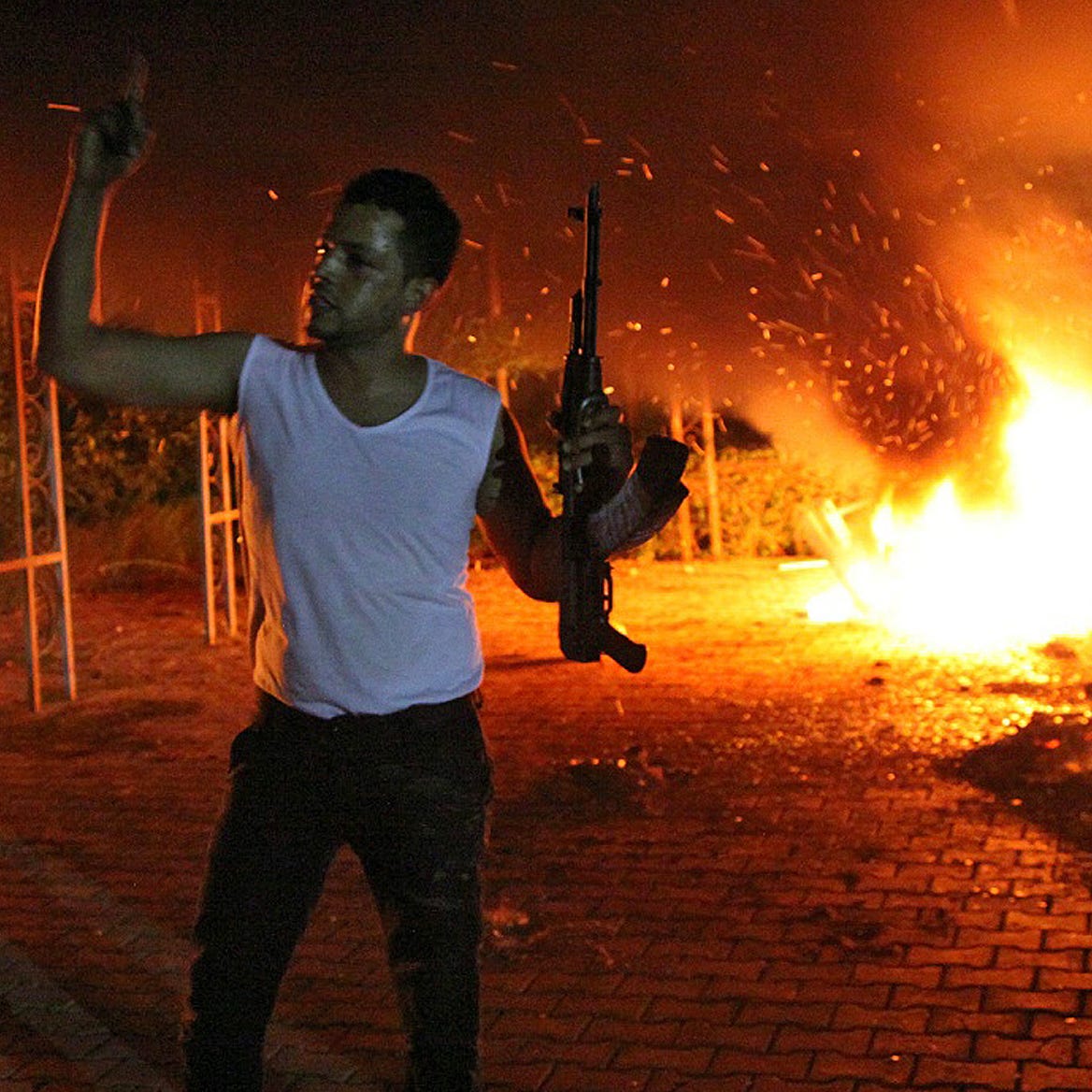 An armed man waves his rifle as buildings and cars are engulfed in flames after being set on fire inside the U.S. consulate compound in Benghazi, Libya late on Sept. 11, 2012.