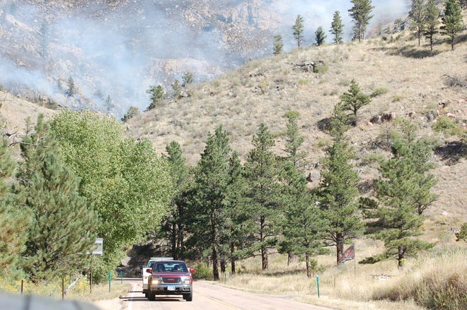Vehicles drive on Colorado Highway 14 with smoke from the Seaman Fire in the background on Wednesday.