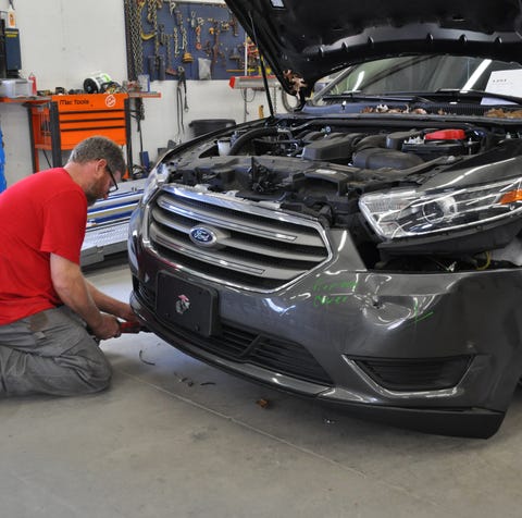 A repair technician removes a car's front bumper...