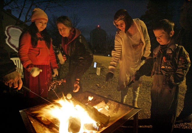 Guests at a past Halloween Family Fun night at the Old Falls Village roast marshmallows around a fire.