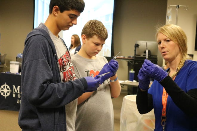 Port Clinton freshmen Zach Adkins and Brandon Fenton listen carefully to the instructions of Kristy Malacos, of Magruder Hospital, on how to draw and administer medication intravenously during the Ottawa County Career Showcase on Friday.