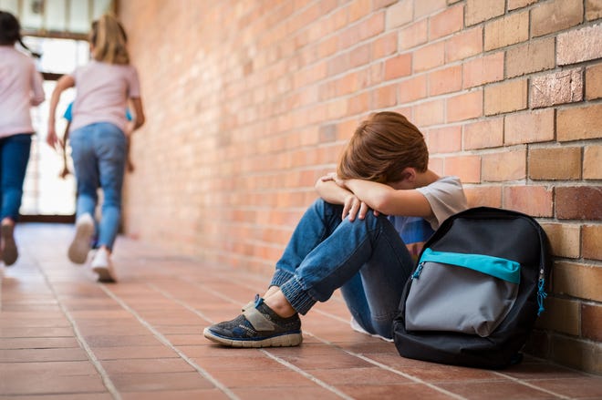 A child is sitting next to a brick wall while two other kids run away.