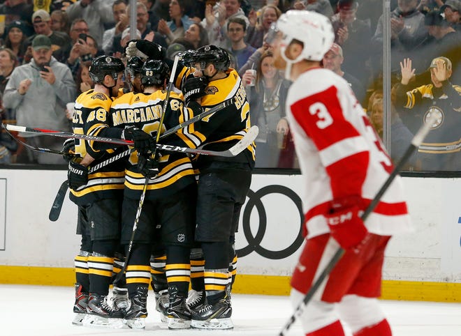 Boston Bruins players surround David Pastrnak after he scored as Red Wings defenseman Nick Jensen looks up earlier this season.