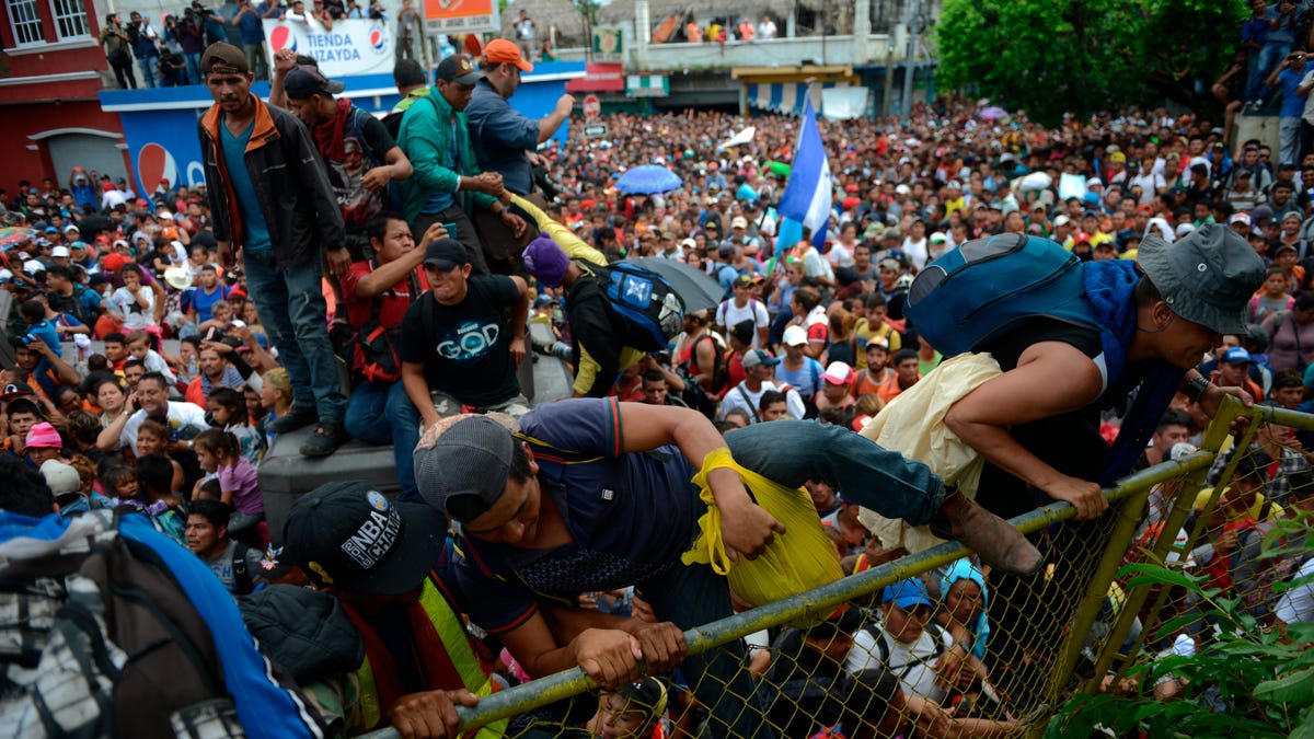 Honduran migrants climb a border fence, in Tecun Uman, Guatemala, Friday, Oct. 19, 2018. Migrants broke down the gates at the border crossing and began streaming toward a bridge into Mexico. After arriving at the tall, yellow metal fence some clambered atop it and on U.S.-donated military jeeps. Young men began violently tugging on the barrier and finally succeeded in tearing it down.