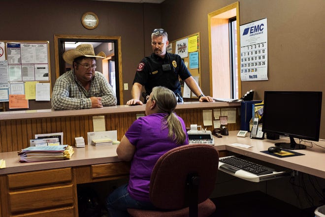 During his shift, Chad Johanning, the chief in Little River, Kansas, discusses the day’s schedule with Sue Peters, the city clerk, and Lucas Baumbach, the city superintendent.
