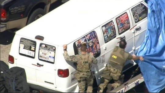 This image capture of a video provided by WPLG-TV shows FBI agents covering a van after the tarpaulin broke off while she was being transported from Plantation, Florida on Friday 26th. October 2018, that federal agents and police officers had interrogated connection with parcel bombs that were sent to high-level critics of President Donald Trump. The van has several stickers on the windows, including American flags, decals with logos and text.