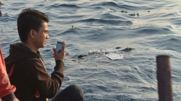 An Indonesian boatman takes pictures as debris...