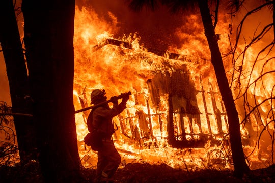 Firefighter Jose Corona sprays water Nov. 9, 2018, as flames consume from the Camp Fire consume a home in Magalia, California.