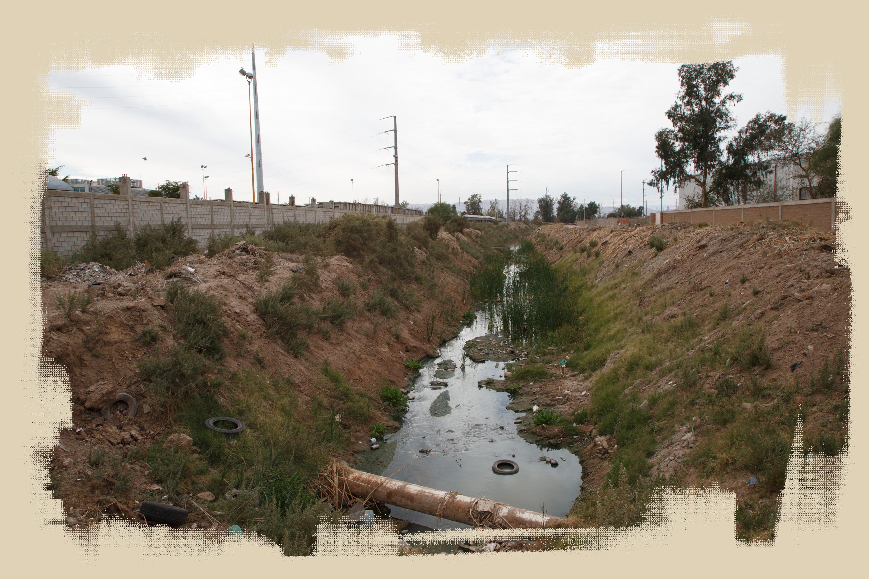 A ditch runs between the Vitro glass factory and a scrapyard in Mexicali. The city’s ditches drain into the New River.