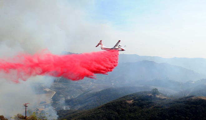 An airplane drops fire retardant on  houses near Mipolomol and Cotharin roads Saturday in the mountains of Ventura County. The Woolsey Fire continues to burn in the county.