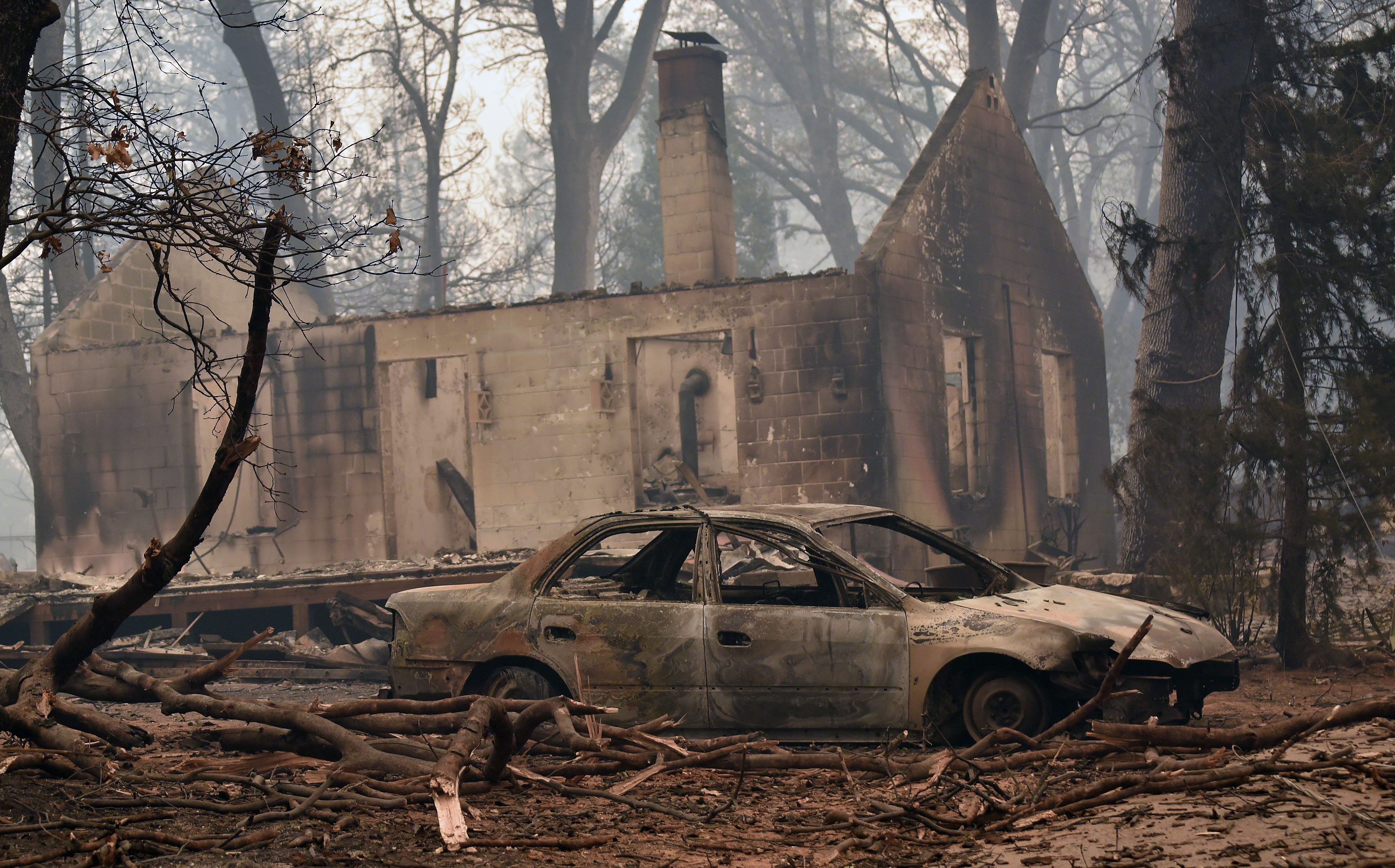 Smoke clouds the air above the remains of a burned-out house and car in Paradise, Calif.