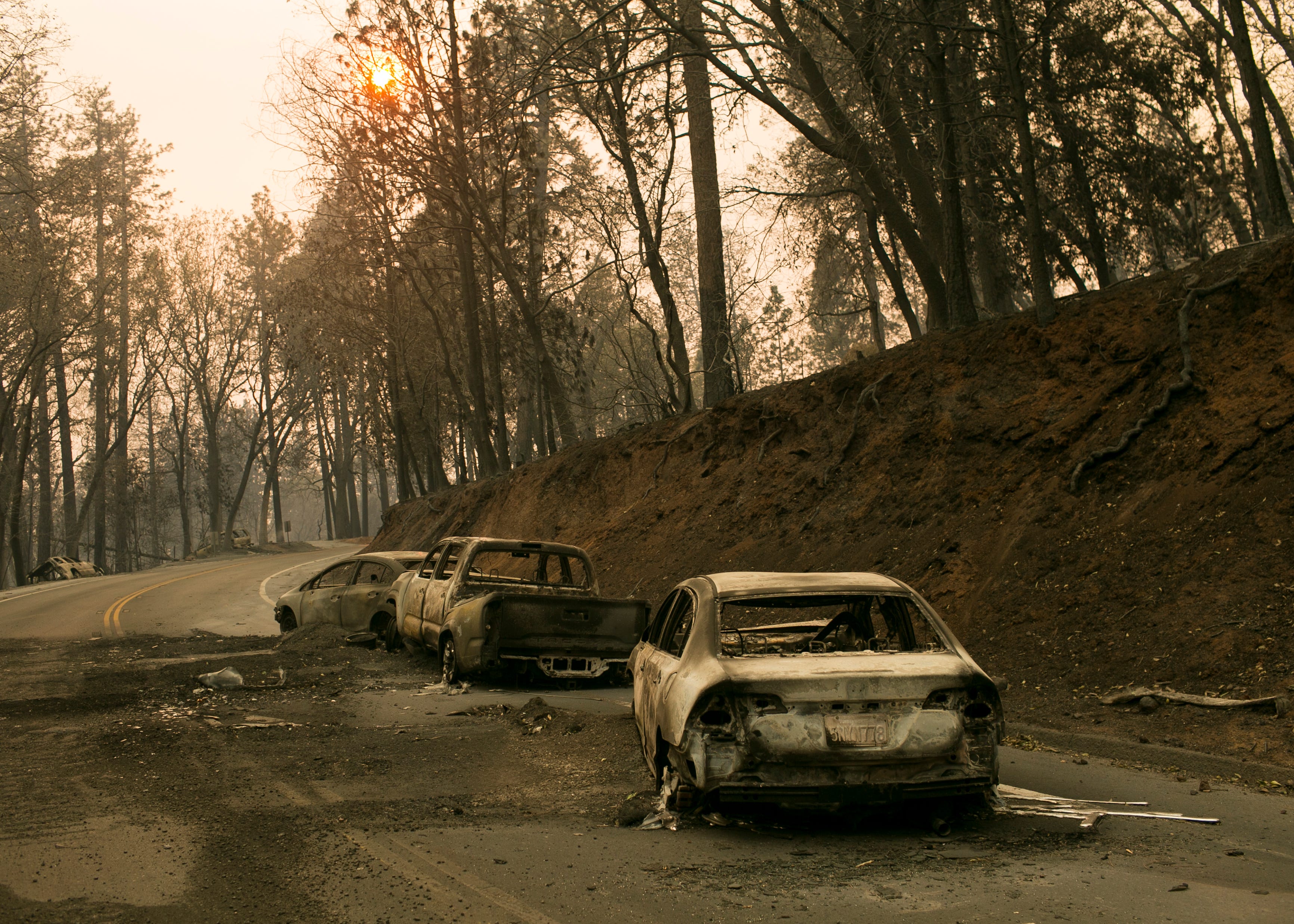 Vehicles sit pushed off the road days after the Camp Fire swept through town on Nov. 11, in Paradise, Calif.