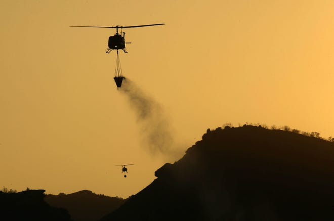 Nov 11, 2018; Westlake Village, CA, USA; A helicopter prepares to drop water on flames from the Woolsey Fire on Nov. 11, 2018, in Westlake Village, Calif. 