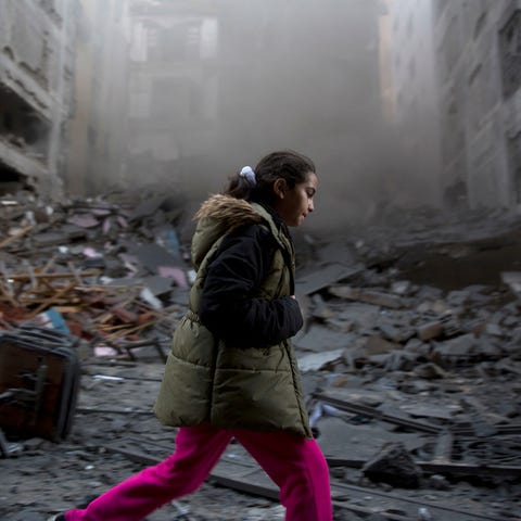 A Palestinian girl walks next to a destroyed...