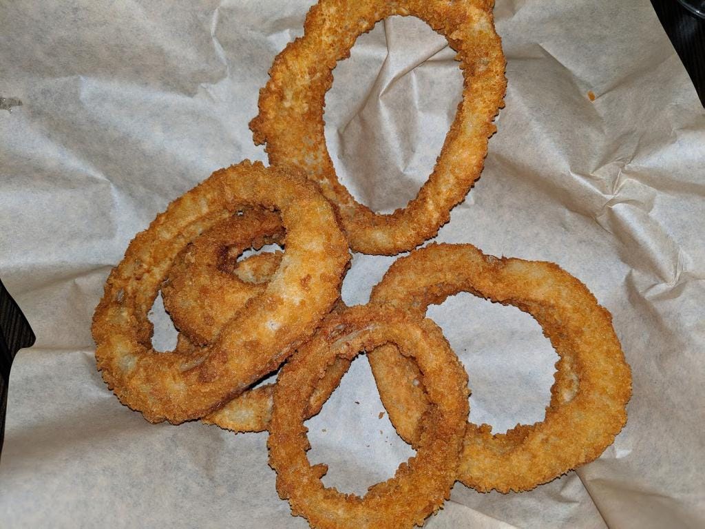 The onion rings at The Angry Goat feature thick onion slices with crisp breading.