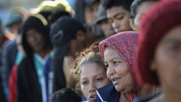 Members of the migrant caravan wait in line to...