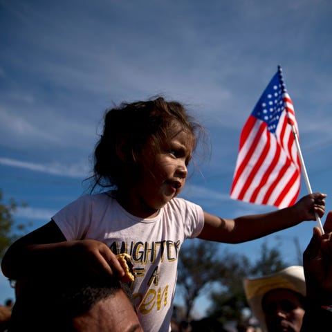 A migrant girl with a U.S. flag sits on the...