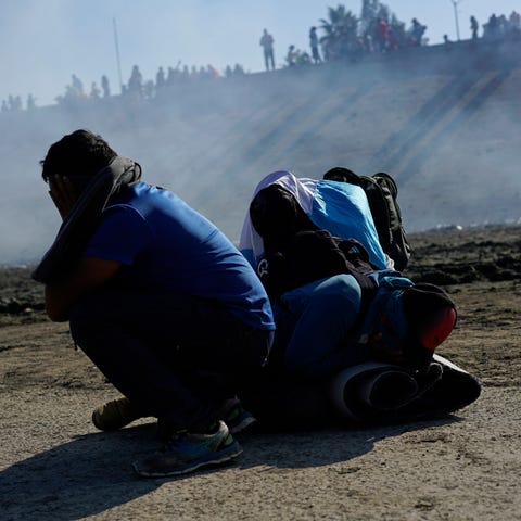 Migrants huddle in the riverbank amid tear gas...