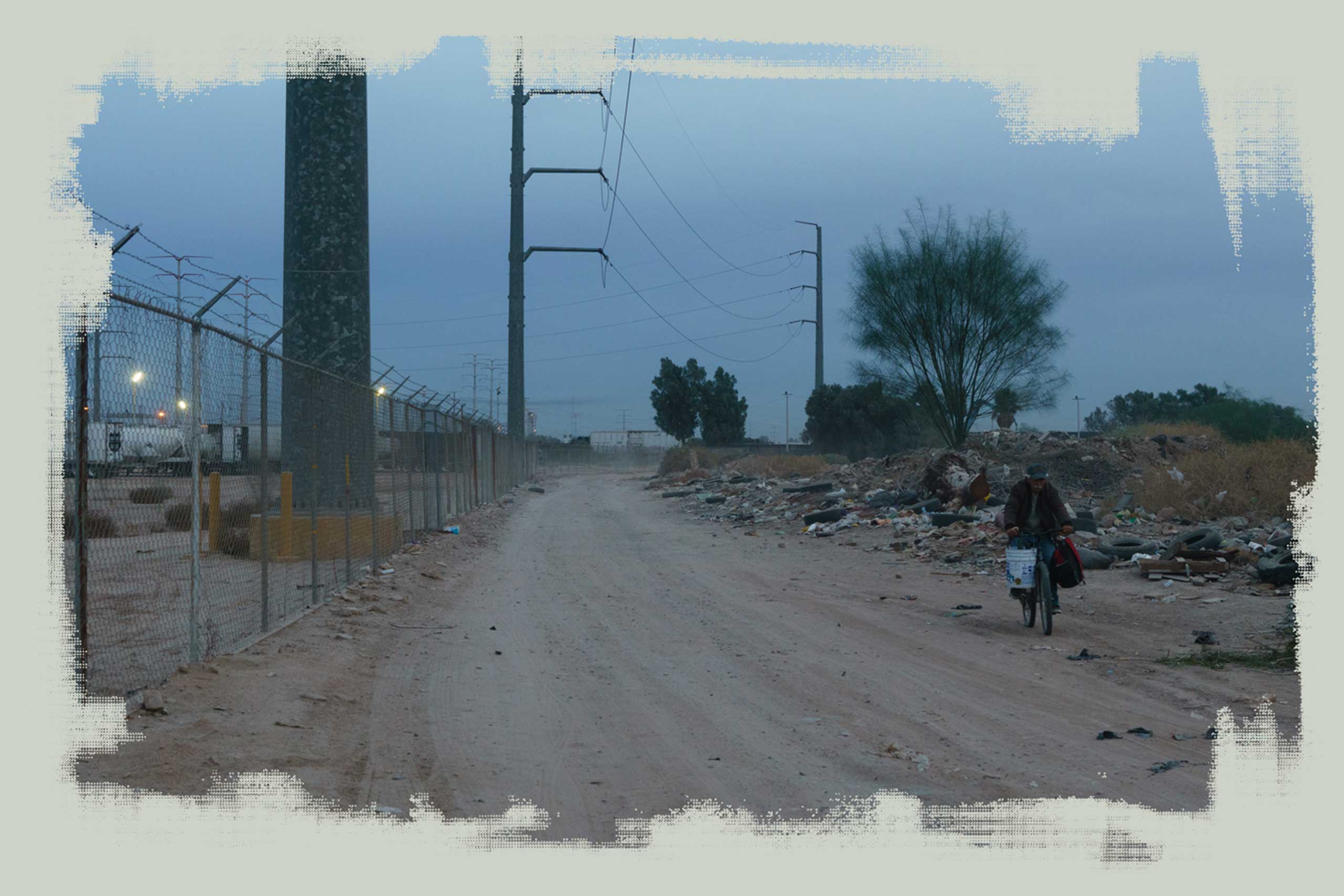 A man rides a bicycle down a road next to a factory in Mexicali.