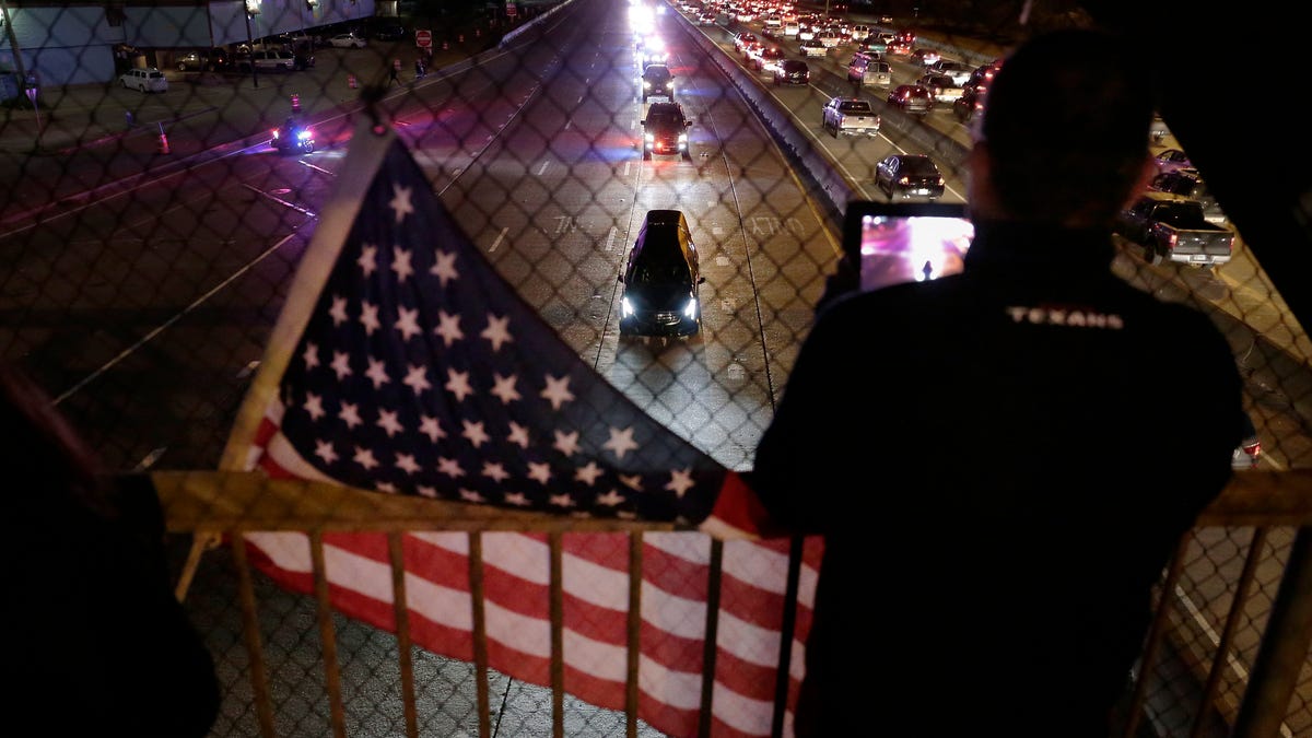 Daniel Medina stands next to his flag on an overpass as he videos the hearse carrying the body of former President George H.W. Bush as it travels to St. Martin's Episcopal Church after returning from Washington D.C.
