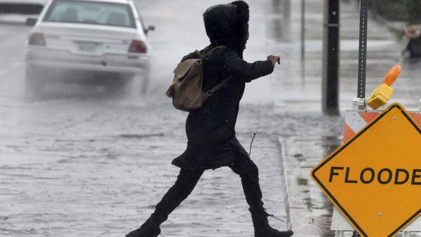 A pedestrian leaps across a flooded portion of...