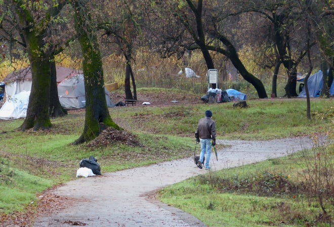 A man walks his dog Monday morning past a row of tents at the Parkview Riverfront Park in Redding.
