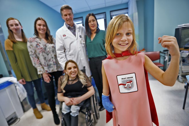 Hayden Cloud, right, strikes a superhero pose, as she stands with Savanna Harrison, from left, Julie-Anne Bignal, Dr. Chuck Dietzen, Amy Duarte, and Kaycee Marshall, front, at Riley Hospital for Children, Thursday, Dec. 20, 2018.  The group has developed superhero outfits, like the one that Hayden is wearing, for Riley kids.