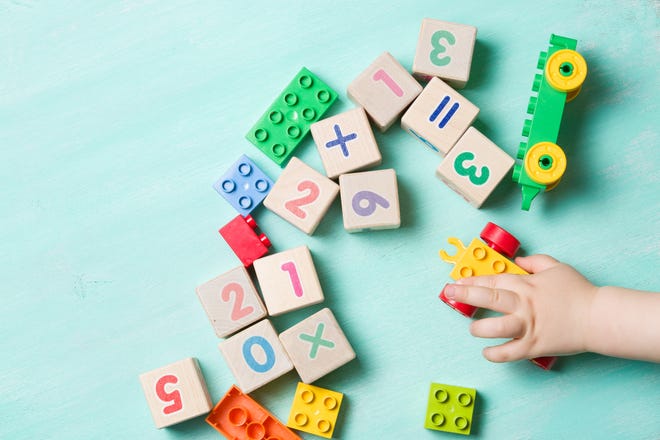 Child playing with wooden cubes with numbers and colorful toy bricks on a turquoise wooden background. Toddler learning numbers. Hand of a child taking toys.