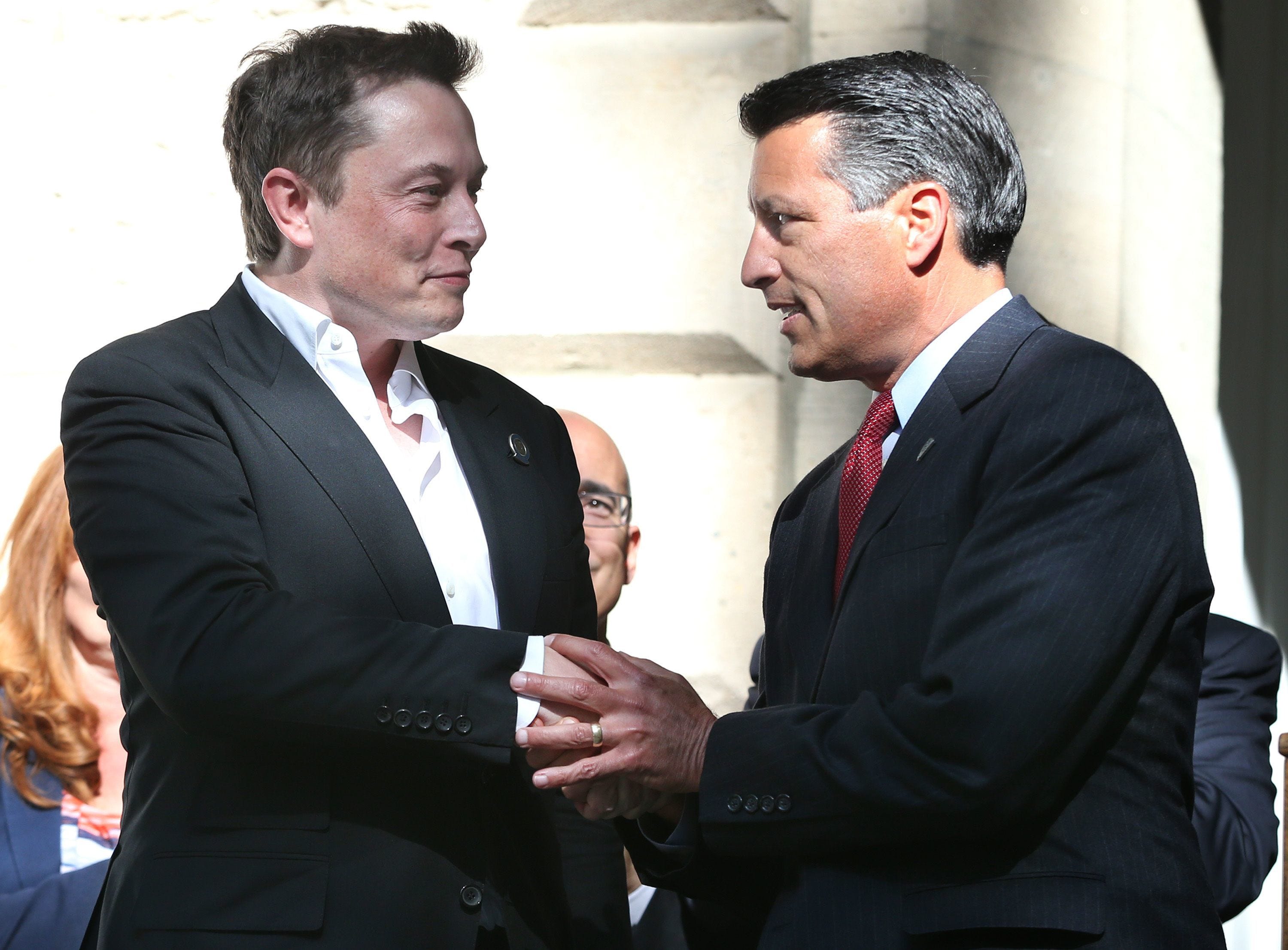 Tesla CEO Elon Musk, left, and former Nevada Gov. Brian Sandoval shake hands following the 2014 announcement that the carmaker would build its $5 billion Gigafactory outside Reno.