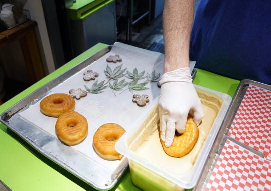 Glazed & Confuzed donuts founder and CEO Josh Schwab frosts a donut with CBD-infused glaze at his shop in the Stanley Marketplace in Aurora, Colorado, before topping each with a candied hemp leaf and gingerbread cutout.


