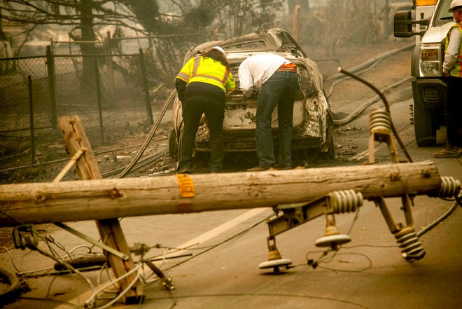 In this Nov. 10, 2018, file photo, with a downed power utility pole in the foreground, Eric England, right, searches through a friend's vehicle after the wildfire burned through Paradise, Calif. To prevent wildfires, Pacific Gas & Electric Co. should re-inspect its entire electric grid and cut off power during certain wind conditions regardless of the inconvenience to customers or loss of profit, a U.S. judge proposed Wednesday, Jan. 9, 2019.