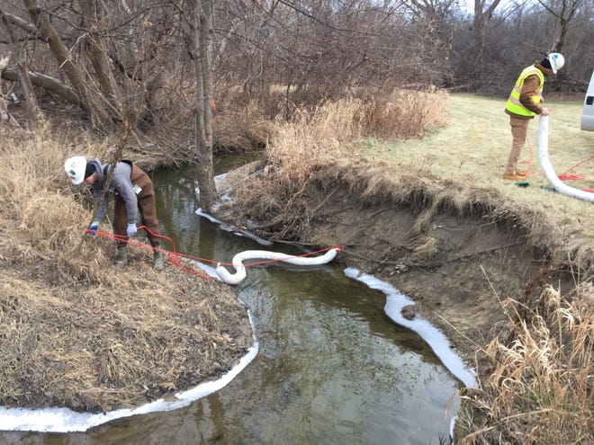 Workers place absorbent blooms in the Plumbrook Drain in Sterling Heights to soak up an oily liquid found in the water.