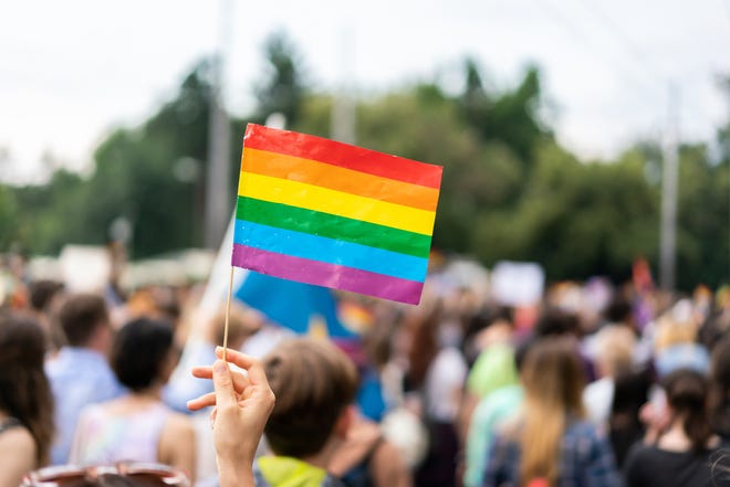 Gay rainbow flag at  gay pride parade with blurred participants in the background