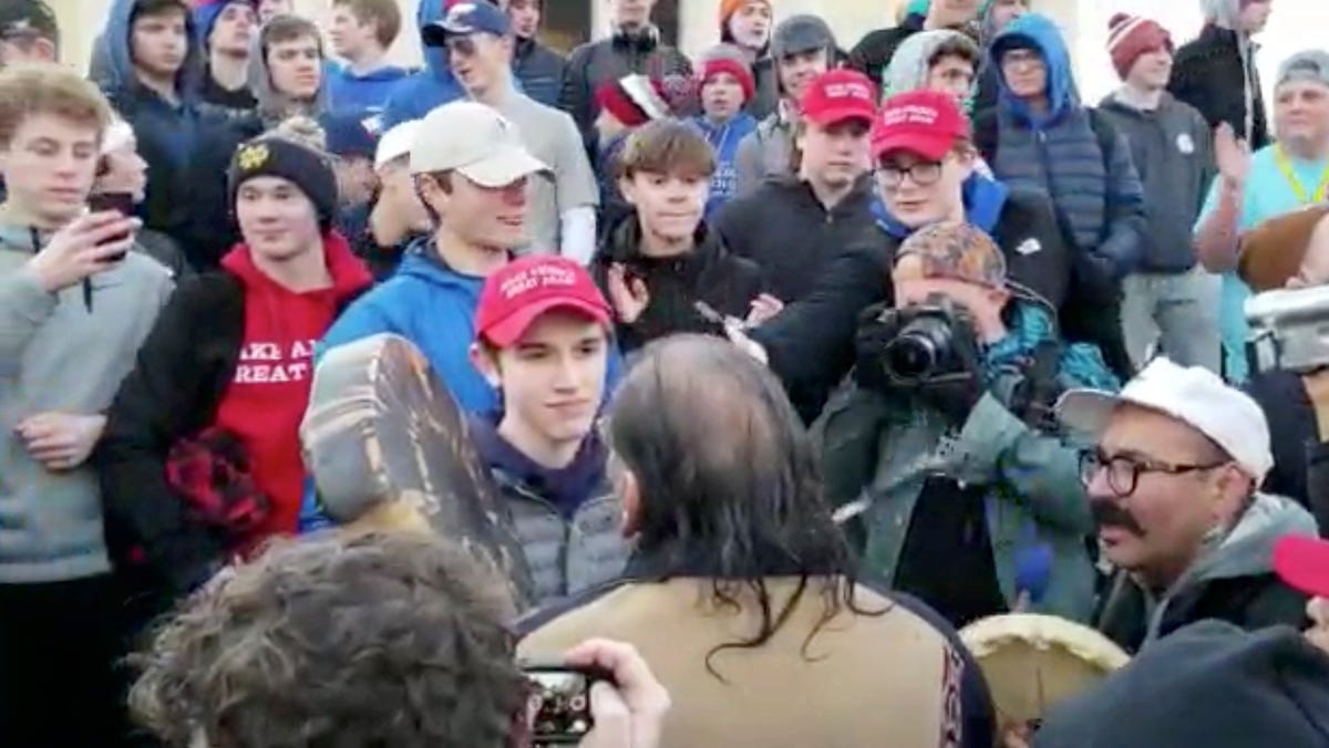 In this Friday, Jan. 18, 2019 image made from video provided by the Survival Media Agency, a teenager wearing a "Make America Great Again" hat, center left, stands in front of an elderly Native American singing and playing a drum in Washington. The Roman Catholic Diocese of Covington in Kentucky is looking into this and other videos that show youths, possibly from the diocese's all-male Covington Catholic High School, mocking Native Americans at a rally   in Washington.