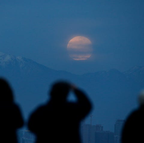 People watch the moon rise behind the downtown...