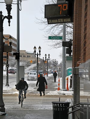Bundled against the cold, pedestrians and a sandwich shop delivery rider make their way under a sign proclaiming a balmy +7 degrees on Tuesday in downtown Lansing.