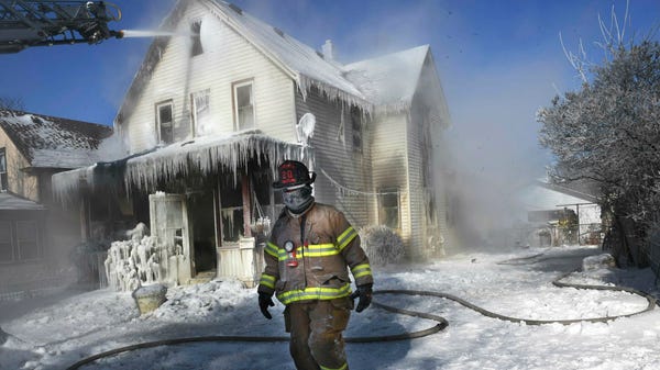 A firefighter walks past an ice-encrusted home...