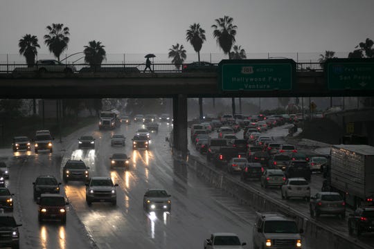 A person walks with an umbrella on a bridge over the 101 Freeway Thursday, Jan. 31, 2019, in Los Angeles, as a storm bears down on California.